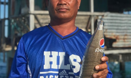 The Philippine fisherman in a blue shirt holds a Pepsi bottle filled with sand.