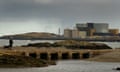 A woman walks her dog on a beach in front of the decommissioned Wylfa nuclear power station on Anglesey