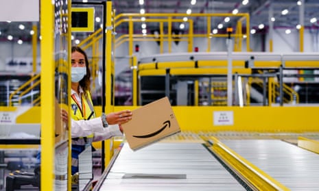 A woman in a facemask places a single Amazon package on an empty conveyor belt at a warehouse in Holland