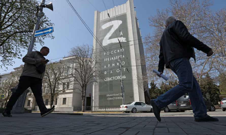 People walk along a street past a banner displaying the “Z” symbol in Sevastopol, Crimea. The banner reads: “For Russia, the president, the army, the navy, Sevastopol.”