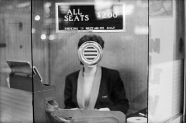 A woman standing inside a ticket booth, with her face obscured by the intercom