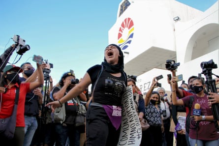 People photograph and film a woman marching down a street carrying a banner.