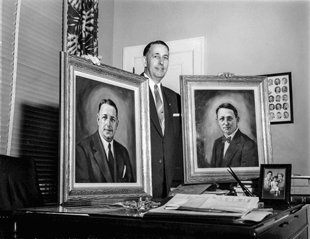 A middle aged man displays two portraits in an office