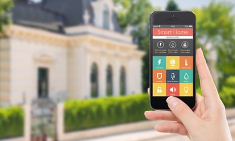 Female hand holding black mobile smart phone with smart home application on the screen. Blurred house on the background. For acc<br>E53FYP Female hand holding black mobile smart phone with smart home application on the screen. Blurred house in the background