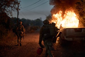 Ukrainian soldiers inspect the burning wreckage of a pick-up truck