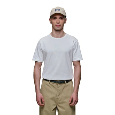 A model wears a white Merz b. Schwanen 2M15 Vintage Machine Refined Classic Fit T-shirt. They also wear a beige baseball cape and chinos.