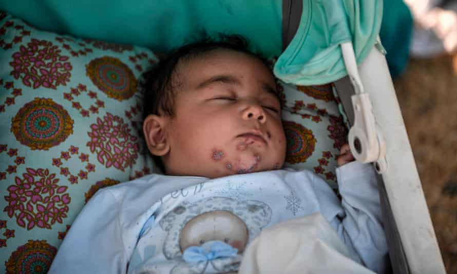 A baby sleeps in a buggy cart along the roadside where thousands of migrants are living without shelter and exposed to the elements near the new temporary camp.