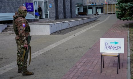An armed Russian serviceman stands guard near a direction sign reading 'referendum' at an outdoor polling station in Mariupol.