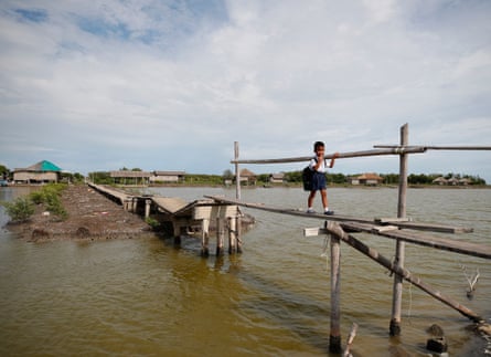 A Thai schoolboy crosses a wooden bridge over invading sea water in Ban Khun Samut Chin