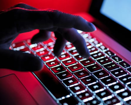 a darkened picture of a hand using a laptop with a red glowing light in the background