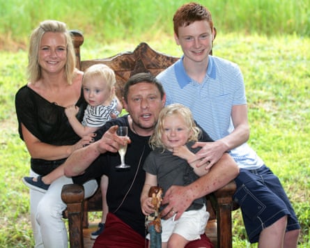 Ryder with his wife, Joanne, and their three children sit on a large chair in a garden