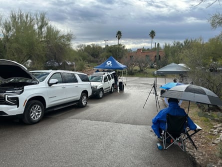 vehicles and people sitting under umbrellas outside a house