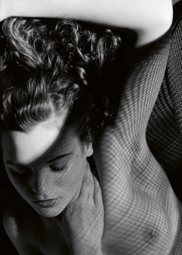Black and white photograph of a topless woman reclining with an arm over her head and mesh shadows falling over her face and torso