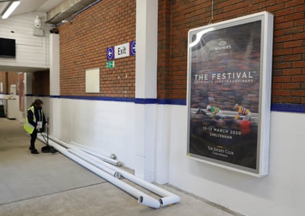 A cleaner sweeps up near spare goal frames stored in the walkway beneath the Whitehorse Lane stand and an advert promotes the Cheltenham Festival before Crystal Palace v Leeds at Selhurst Park on 7 November.