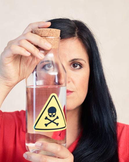 A woman with dark hair holding a bottle with clear liquid in and a yellow toxic sticker on the front