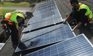 Two men in high vis vests installing solar panels on a roof