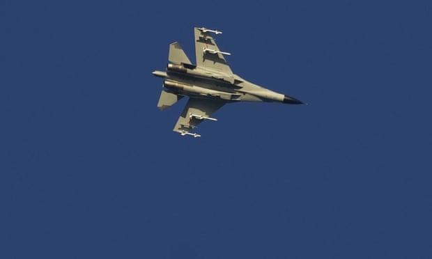 A military fighter jet seen from below against a blue sky