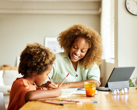 Happy mother helping son doing homeworkCheerful businesswoman with curly hair helping son doing homework. Happy mother is assisting boy while sitting at table. They are at home.