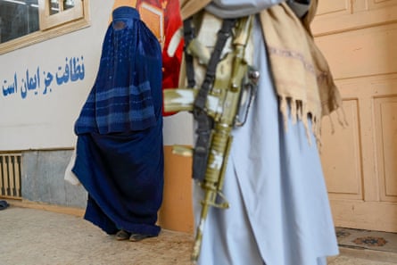 a women in a hijab next to a man with an assault rifle