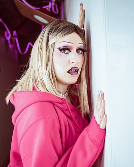Heavily made up drag performer in a blond wig and pink hoodie
