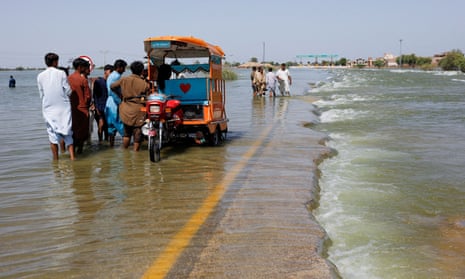 Displaced people stand on a flooded highway, following rains and floods during the monsoon season in Sehwan, Pakistan.