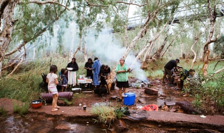 Treize membres de la communauté Yindjibarndi préparent de la nourriture et mangent près d'un feu de camp près d'un ruisseau 
