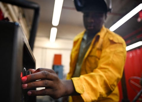 Tyrion Davis, wearing a welder’s mask, adjusts a dial on the side of a piece of equipment qhxidiqxkiqdhinv