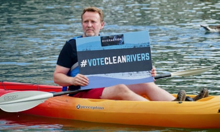 A man in a canoe on the river holds up a sign saying #VoteCleanRivers
