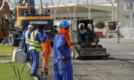 Men wearing hard hats, hi-vis vests and scarves around their faces work on laying a road surface in Qatar.