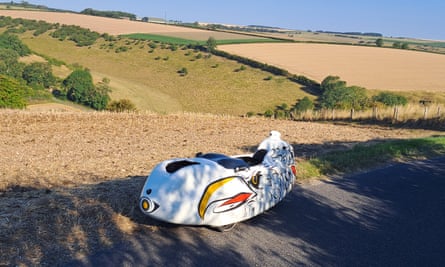 The white velomobile, which is a plastic shell wrapped around a seat and three wheels. It has an illustration of an eagle’s head on its side. 