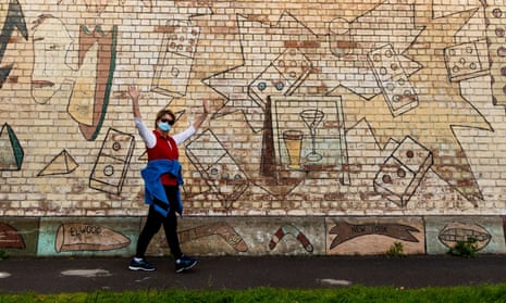 Masked woman walking past graffitied wall