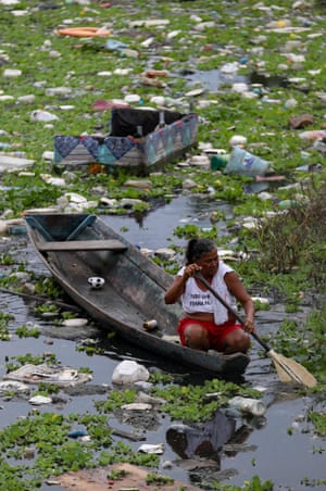 Uma mulher recolhe latas de alumínio no córrego Educandos em Manaus, Brasil