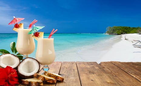 Two glasses of piña colada on wood table shot against tropical beach background