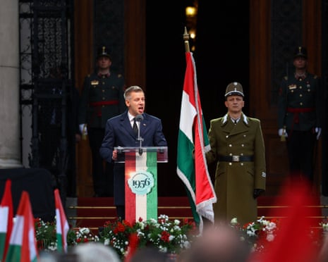 Péter Magyar delivers a speech in Budapest on Friday to mark the 70th anniversary of the Hungarian Uprising of 1956. He stands at a podium with people in the crowd holding Hungarian flags.