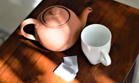 Teapot, mug and teabags sit on a wooden table