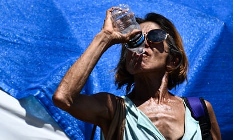 A woman drinks a bottle of water while walking in ‘The Zone’, a vast homeless encampment, in Phoenix, Arizona