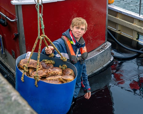 A young man loads a bucket of crabs off a fishing trawler