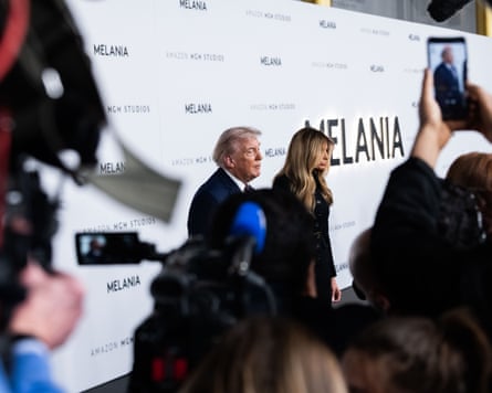 a man and a woman on a red carpet as photographers take picture