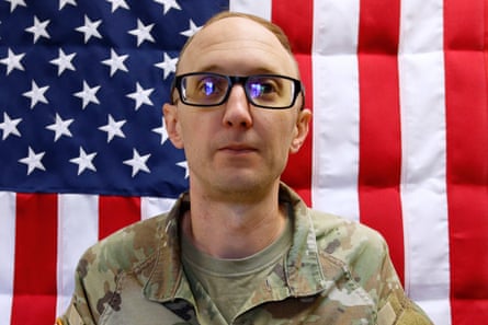 a soldier stands in front of a US flag