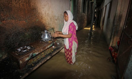 A woman cooks outside her home in a flooded corridor of Sylhet, Bangladesh, following heavy rains