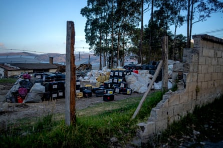 A pile of full plastic containers and bags in a field behind a fence