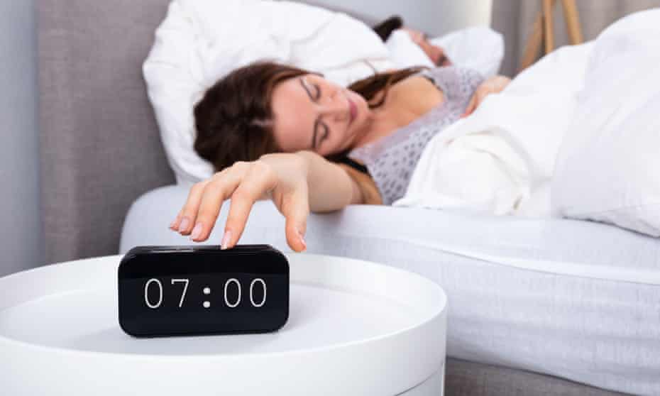 Young Woman Sleeping On Bed Turning Off Alarm Clock In Bedroom