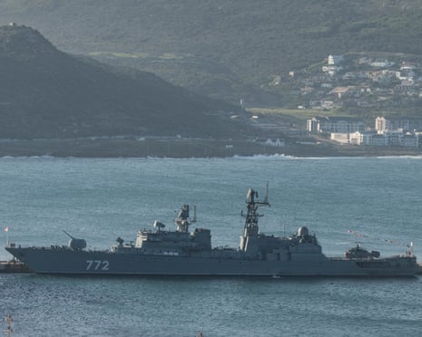 Russian Navy frigate Neustrashimy marked with number 772 sits in calm blue water with hills and coastal buildings in the background