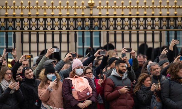 Two women wearing protective face masks stand amongst tourists outside Buckingham Palace
