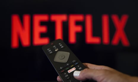 A person holds a remote control in front of a Netflix logo