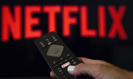 A person holds a remote control in front of the Netflix logo