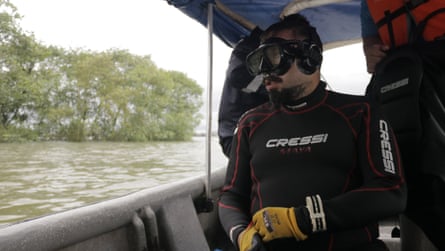 A man wearing scuba diving gear looks out across the water from a boat