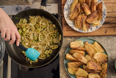 Sebuah tangan mengaduk tumis bawang bombay dan adas cincang, dengan irisan adas goreng di atas piring di sampingnya.
