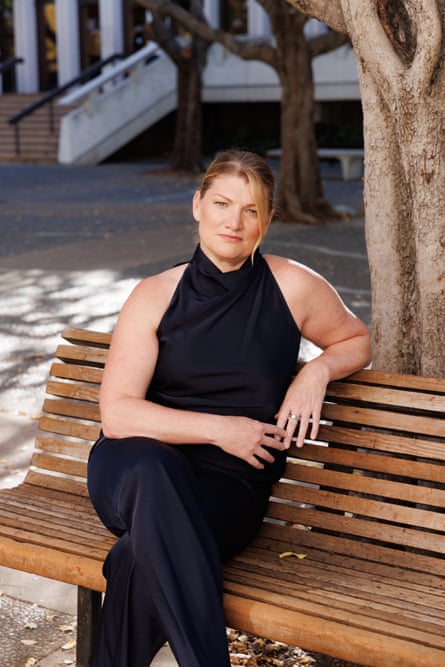 Candice Odgers, in a black halterneck top and black trousers, sits on a wooden bench in front of a tree on the campus of the University of California, Irvine