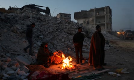 People warm themselves around a fire near collapsed building after an earthquake in Idlib, Syria.